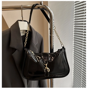 Detail of glossy black patent leather bag featuring golden chain strap and buckle closure