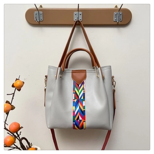 Detail der grauen Ledertasche mit buntem Webstreifen und braunem Griff am Holzhaken