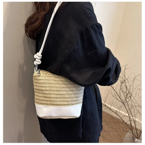 Detail view of woven straw bucket bag with white leather base and knot shoulder strap