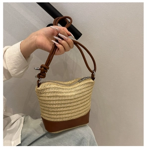 Detail of handwoven straw bucket bag with brown leather bottom and thin shoulder strap
