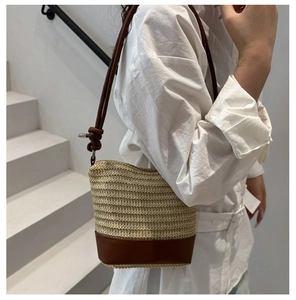 Detail of woven straw bucket bag with dark brown leather base and slim shoulder strap