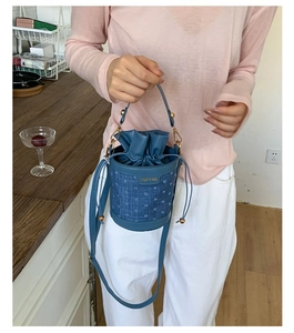 Detail of blue fabric bucket bag with leather trim and gold hardware in hand