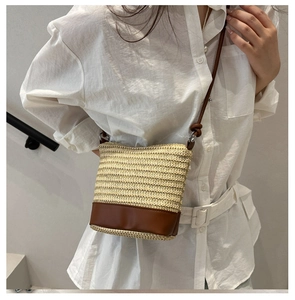 Close-up of woven straw bucket bag with brown leather trim and slim shoulder strap