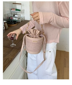 Detailed close-up of a pink drawstring bucket bag featuring a textured fabric and gold label