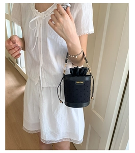 Detail of black bucket bag with textured dot pattern and satin drawstring closure