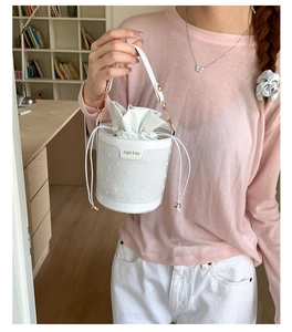 Detail of white bucket bag featuring textured leather, drawstring closure and gold hardware
