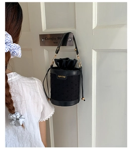 Detail of black bucket bag with 3D polka dot texture and drawstring satin inner bag
