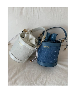 Detail of bucket bag showing contrast colors, drawstring closure and gold brand logo