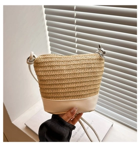 Detail of straw woven bucket bag with white leather base and thin shoulder strap