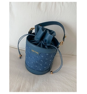 Close-up of blue denim bucket bag with texture dots, gold hardware, and leather drawstring