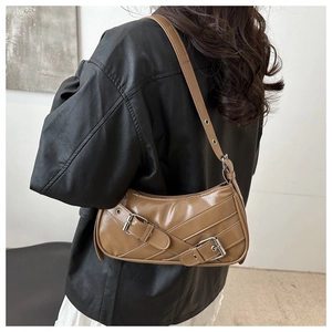 Close-up of brown pleated shoulder bag with metallic buckles worn by a model