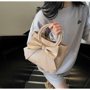 Détail d'un sac à main beige avec nœud élégant, lettrage doré et poignée ronde