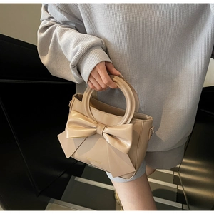 Détail du sac beige en similicuir avec grand nœud décoratif et poignée ronde rigide