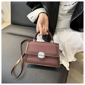 Detail van crossbodytas met bordeaux geweven textuur, bruin leer en een zilveren gesp