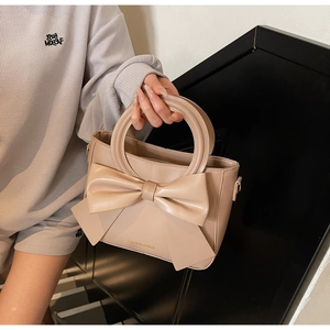 Détail d'un sac beige avec grand nœud décoratif et poignées circulaires uniques