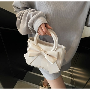 Détail du sac crème avec nœud décoratif, poignée ronde et logo FASHION & BAGS