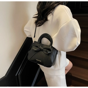 Detail of black bow-knot tote bag with adjustable strap worn by model on stairs