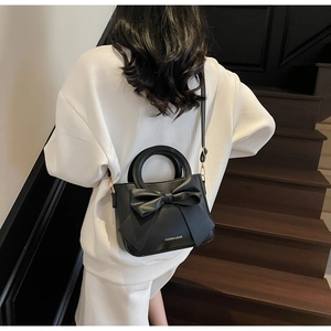 Vue détaillée d'un sac à main noir à nœud avec finitions dorées sur un escalier en bois