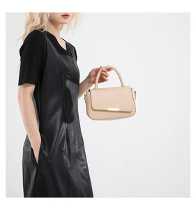 Détail du sac à main beige clair avec finitions dorées tenu par un mannequin en robe