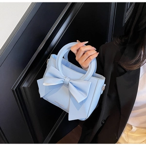 Détail du sac à main bleu clair avec nœud, poignée ronde et logo doré