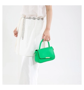 Détail du sac à main vert en cuir avec barre dorée et poignée, porté par un mannequin