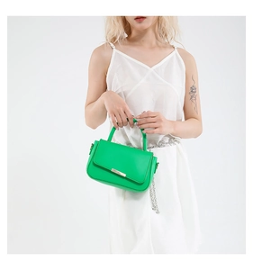 Sac à main en cuir vert avec fermoir doré et bandoulière chaîne sur fond blanc