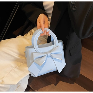 Détail d'un sac à main bleu clair avec un grand nœud décoratif et une poignée ronde