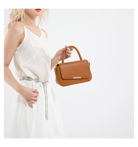 Detailansicht der braunen Ledertasche mit rechteckiger Metallplakette und rundem Tragegriff