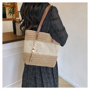 Détail du sac cabas en paille tressée avec larges rayures, lanières en cuir et pompon