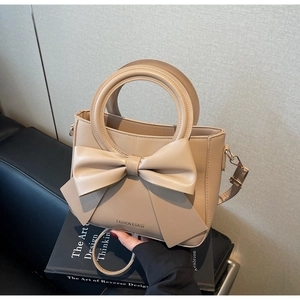 Detail of beige square bag featuring a large bow and circular handle on books