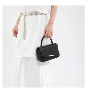 Detail einer schwarzen Lederhandtasche mit Goldleiste und elegantem weißem Kleid