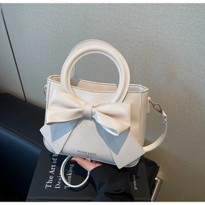 Detail of cream white handbag featuring a large bow and a circular metal handle