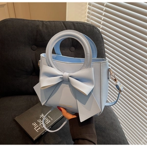 Détail d'un sac à main bleu clair avec un nœud décoratif et une inscription dorée