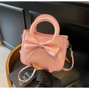 Détail d'un sac à main rose avec un grand nœud en cuir et inscription dorée chic