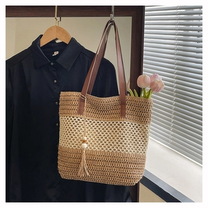 Détail du sac cabas en paille tressée avec anses en cuir marron et pompons en bois