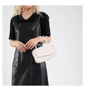 Sac à main beige chic avec boucle dorée porté par un mannequin en robe de cuir noir