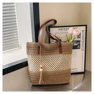 Gros plan sur un sac cabas bicolore en paille avec bandoulière en cuir et gland décoratif