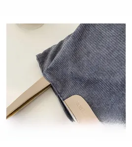 Detail of grey corduroy tote bag featuring a leather fashion patch and strap texture
