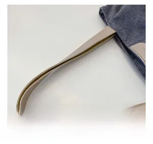 Close-up of wide cream leather handle with neat stitching on blue corduroy tote bag