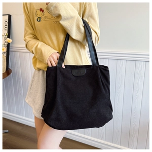 Detail of black corduroy tote bag featuring a leather strap and FASHION logo patch