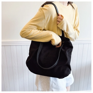 Close-up of black corduroy tote bag featuring striped texture and shoulder strap on model