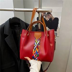 Red leather tote bag with ethnic woven strap and decorative geometric pattern detail