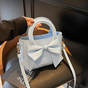 Sac à main bleu clair avec grand nœud et poignée ronde, présenté sur un siège chic