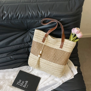 Sac cabas en paille rayé avec poignées marron et pompon posé sur un canapé