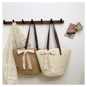 Détail de sacs en paille tissée avec nœuds en dentelle crème et anses en cuir brun