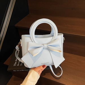 Sac à main bleu clair avec nœud, poignée ronde et bandoulière sur des marches en bois