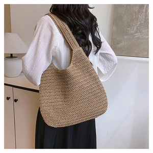 Detail of a large straw tote bag with woven texture worn over the shoulder by a model