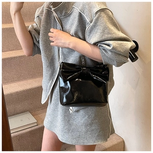 Detail of black patent leather tote bag with oversized bow and metal chain strap