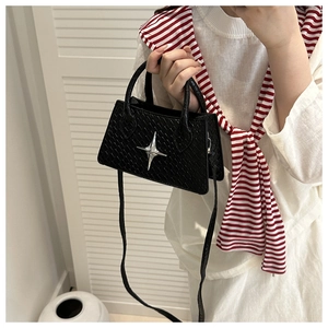 Detail of woven texture shoulder bag with silver star emblem and slender crossbody strap