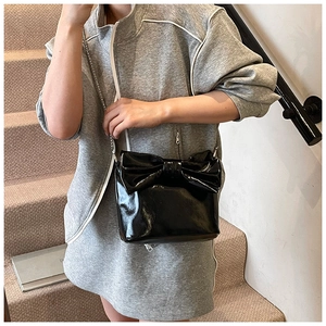 Detail of glossy black patent leather tote bag with oversized 3D bow and silver chain strap